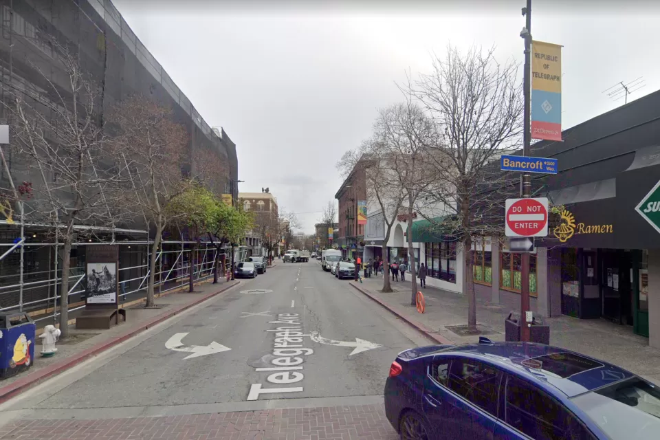 A narrow, one-way street is lined with businesses.